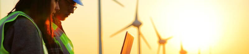 2 people looking at a laptop outside in front of wind turbines