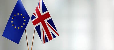 European-Union-And-British-Flag-Pair-On-A-Desk-Over-Defocused-Background