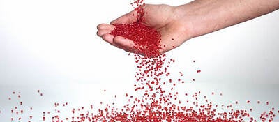 A hand catching red plastic pellets