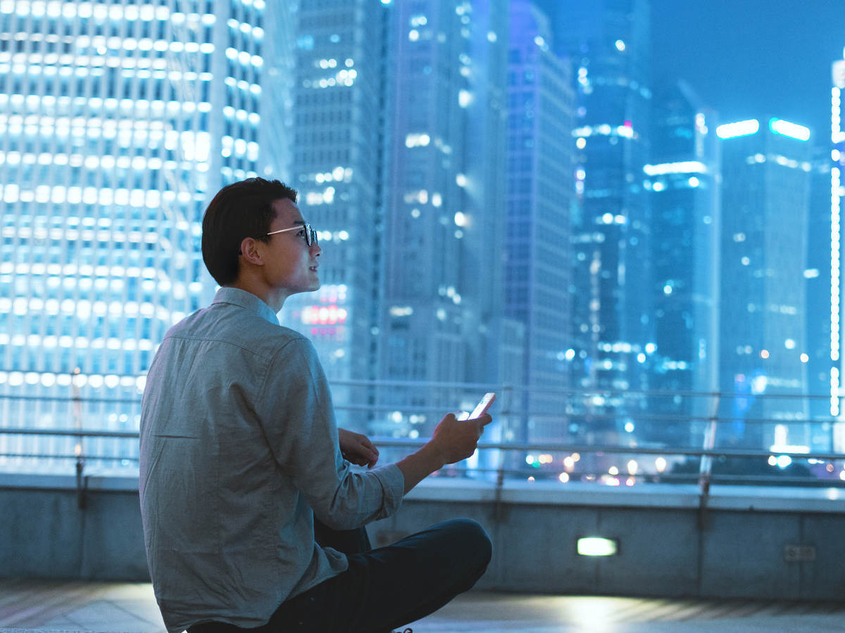 Man siting on roof of building holding smartphone