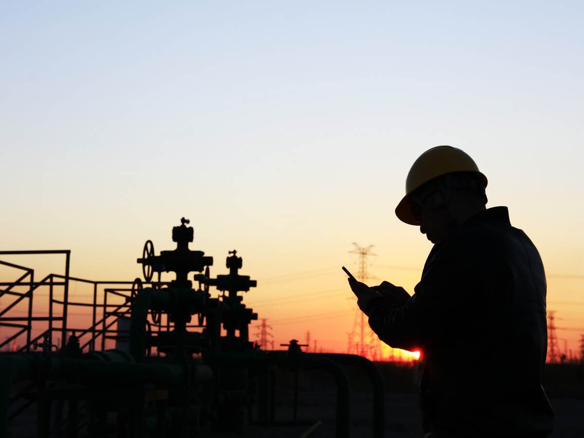 Worker in an oil field at sunset using mobile device